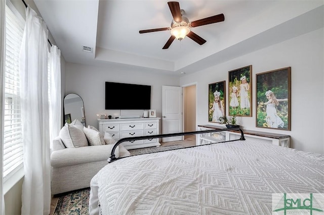 bedroom with a raised ceiling, visible vents, and ceiling fan