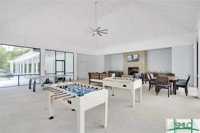 recreation room featuring high vaulted ceiling, a brick fireplace, concrete flooring, and a ceiling fan