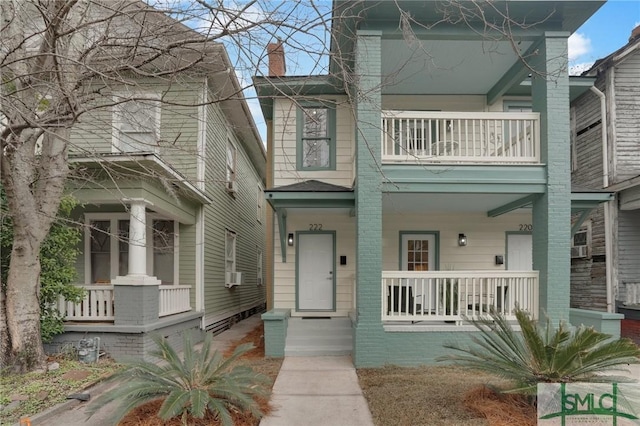 view of front of house featuring a porch, a chimney, a balcony, and brick siding
