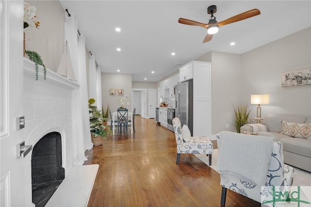 living area with light wood-style floors, ceiling fan, a fireplace with raised hearth, and recessed lighting