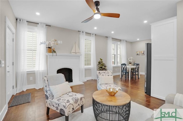 living room featuring a ceiling fan, wood finished floors, a fireplace with raised hearth, recessed lighting, and baseboards