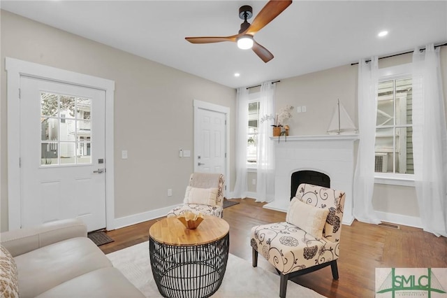 living area with wood finished floors, a ceiling fan, healthy amount of natural light, a fireplace with raised hearth, and recessed lighting