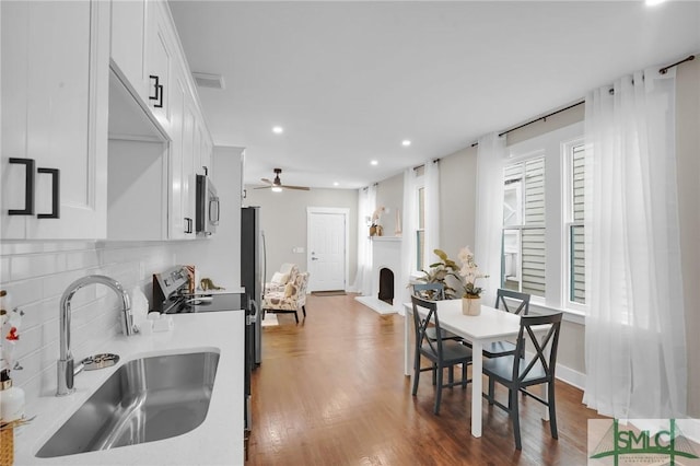 kitchen with a sink, appliances with stainless steel finishes, white cabinetry, light countertops, and wood finished floors