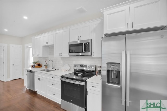 kitchen with appliances with stainless steel finishes, a sink, light countertops, decorative backsplash, and white cabinets