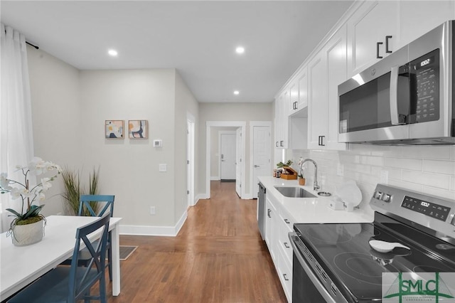 kitchen with stainless steel appliances, a sink, decorative backsplash, dark wood-type flooring, and light countertops