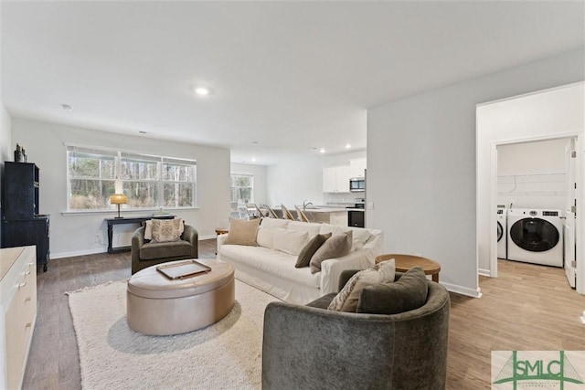 living area featuring light wood-style floors, washing machine and dryer, baseboards, and recessed lighting