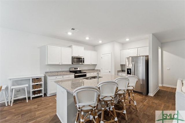 kitchen with stainless steel appliances, white cabinets, an island with sink, and light stone countertops