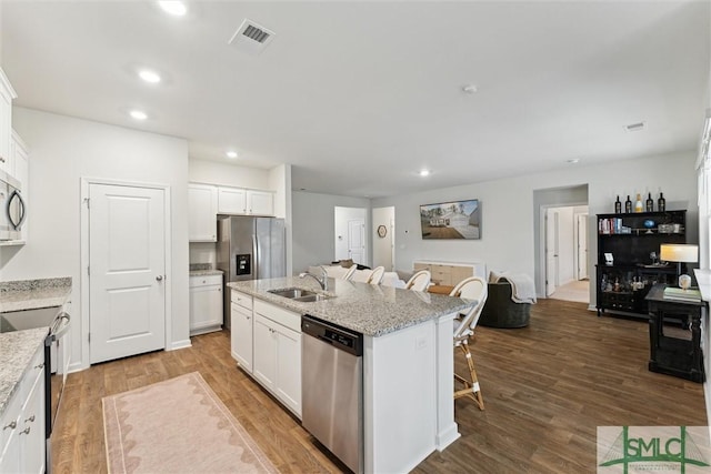 kitchen with light stone counters, a kitchen island with sink, stainless steel appliances, a sink, and white cabinets