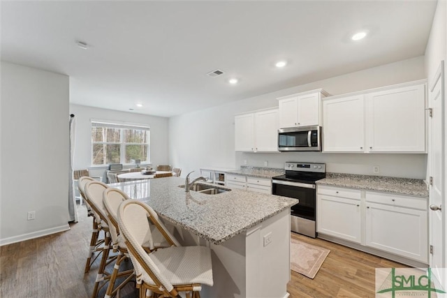 kitchen with a kitchen island with sink, stainless steel appliances, a sink, visible vents, and white cabinets