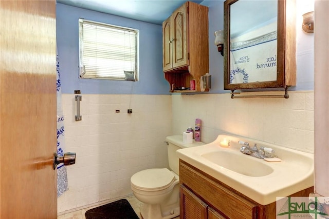 half bathroom with wainscoting, toilet, tile walls, and vanity