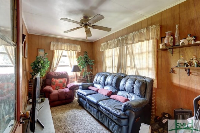 carpeted living room featuring ceiling fan, wooden walls, and crown molding