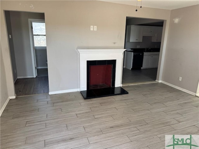 unfurnished living room with wood tiled floor, baseboards, a fireplace with raised hearth, and a sink