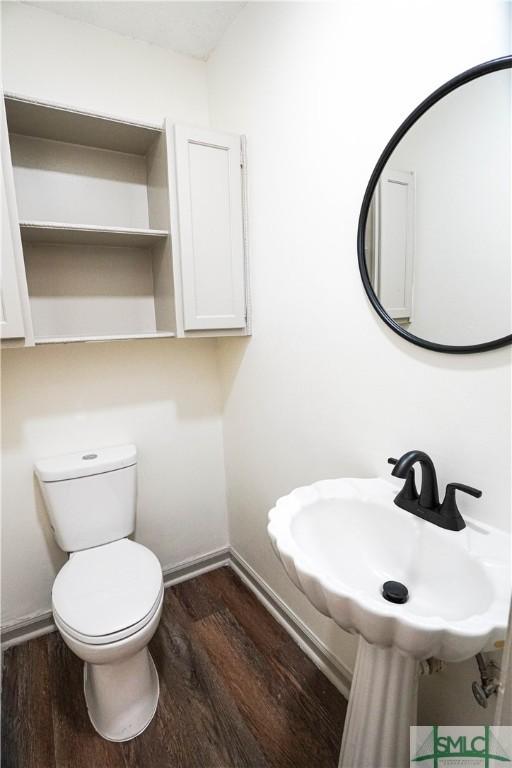 half bathroom with toilet, a sink, baseboards, and wood finished floors