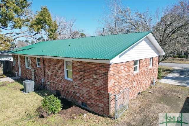 view of side of property with metal roof, central AC, and brick siding