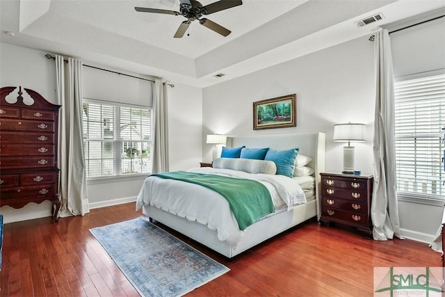 bedroom with dark wood-type flooring, a tray ceiling, visible vents, and multiple windows