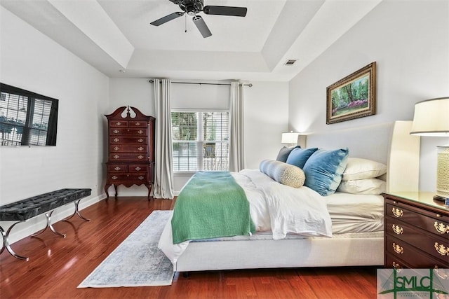 bedroom with dark wood-style floors, a raised ceiling, visible vents, and baseboards