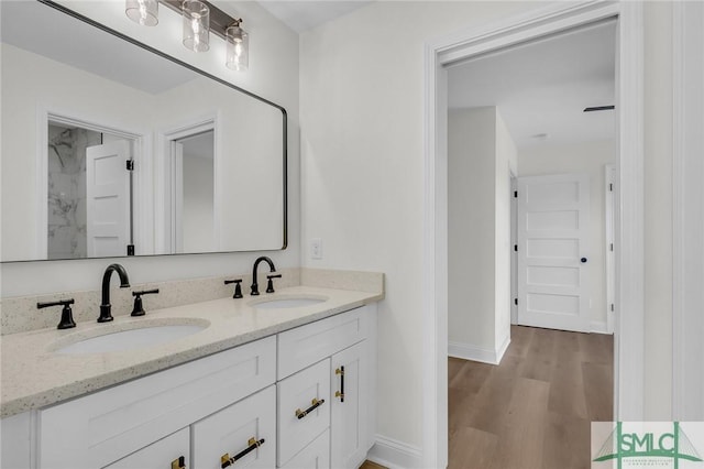 bathroom featuring double vanity, wood finished floors, a sink, and baseboards