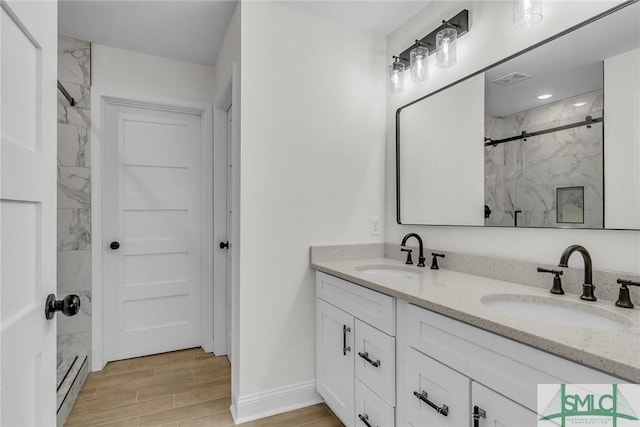 bathroom featuring wood finish floors, a sink, a marble finish shower, and double vanity