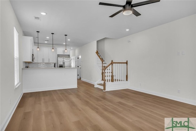 unfurnished living room with light wood-type flooring, visible vents, baseboards, and stairs