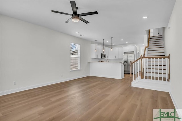 unfurnished living room with light wood-style floors, stairs, baseboards, and a ceiling fan