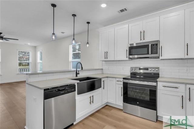 kitchen with a peninsula, a sink, white cabinetry, hanging light fixtures, and appliances with stainless steel finishes