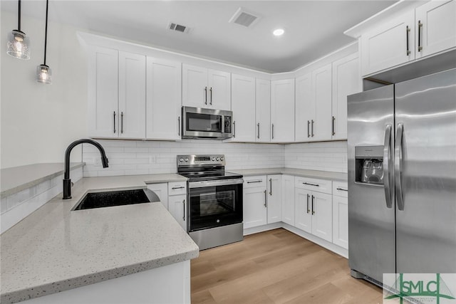 kitchen with stainless steel appliances, white cabinetry, hanging light fixtures, and a sink