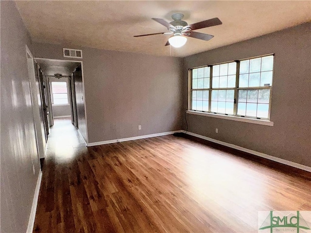 empty room featuring dark wood-type flooring, visible vents, baseboards, and a ceiling fan