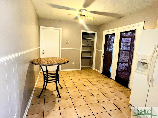 interior space with a wainscoted wall, light tile patterned floors, a ceiling fan, and a textured ceiling