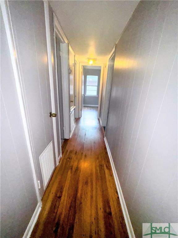 corridor featuring baseboards, visible vents, and dark wood-type flooring