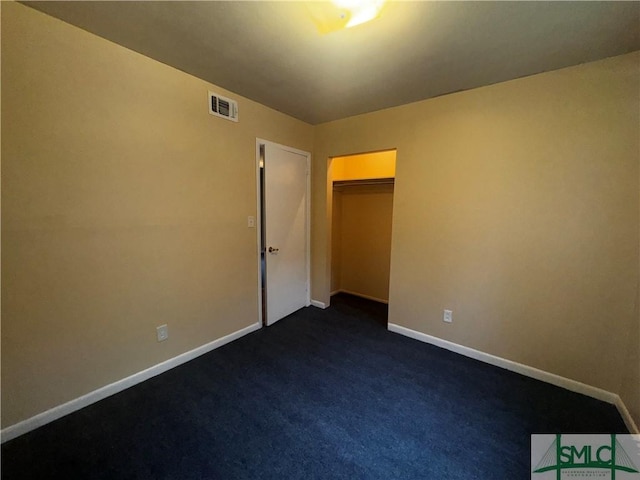 spare room with dark colored carpet, visible vents, and baseboards