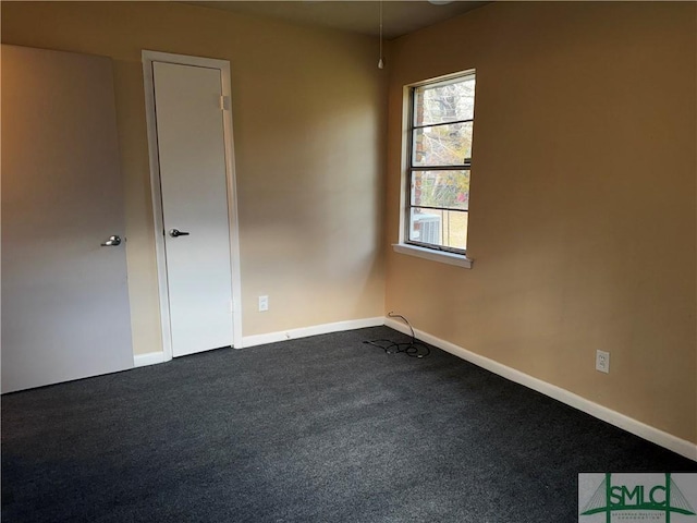 empty room featuring dark colored carpet and baseboards