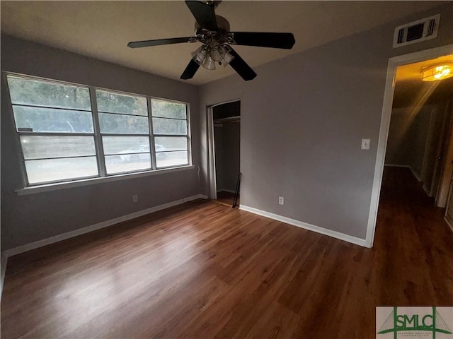 unfurnished bedroom featuring dark wood-style flooring, a closet, visible vents, ceiling fan, and baseboards