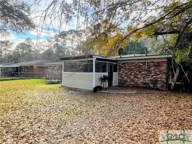 rear view of house featuring a yard, a sunroom, brick siding, and fence