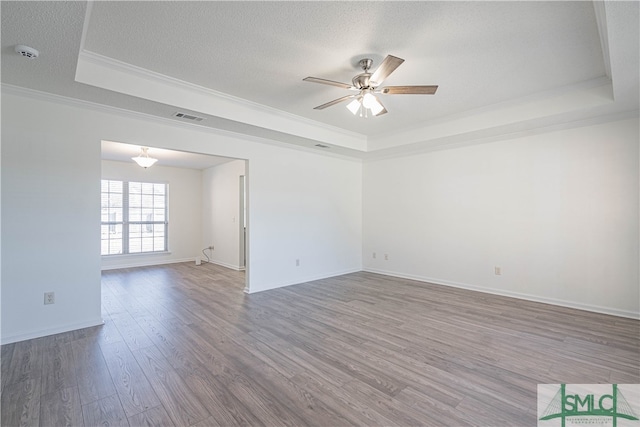 spare room featuring a textured ceiling, wood finished floors, visible vents, a raised ceiling, and crown molding