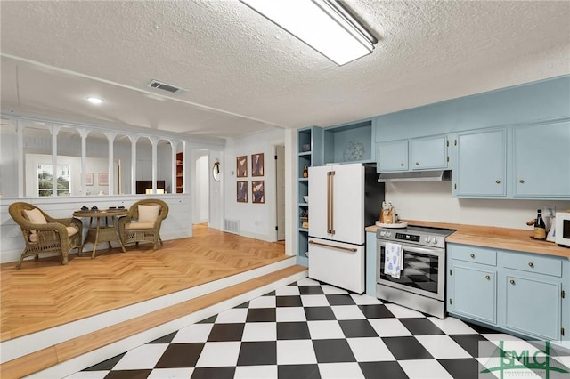 kitchen featuring dark floors, under cabinet range hood, visible vents, freestanding refrigerator, and stainless steel range with electric stovetop