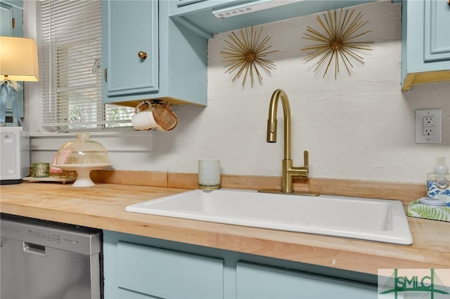 kitchen with dishwasher, butcher block countertops, a sink, and blue cabinets