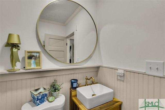 half bath featuring toilet, vanity, crown molding, and wainscoting