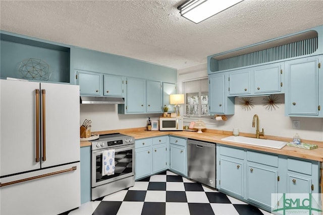 kitchen with dark floors, appliances with stainless steel finishes, a sink, blue cabinets, and under cabinet range hood