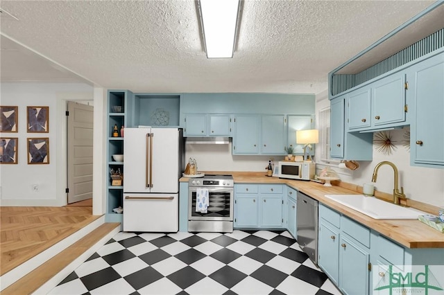 kitchen with butcher block counters, dark floors, stainless steel appliances, open shelves, and a sink