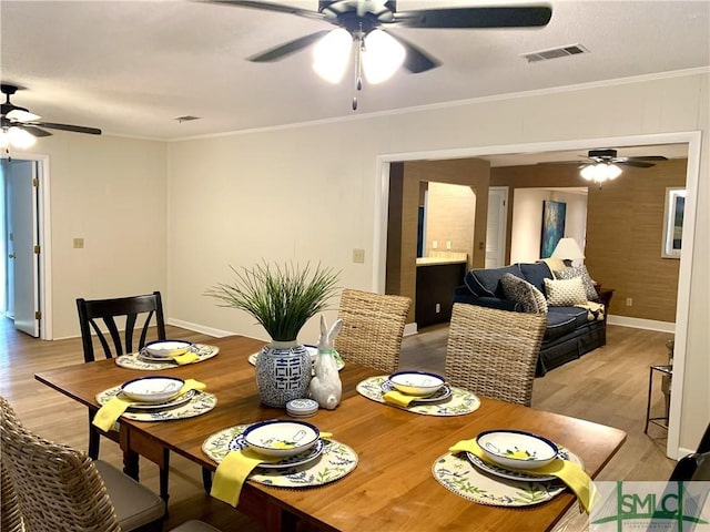 dining space featuring ornamental molding, light wood-style flooring, visible vents, and baseboards