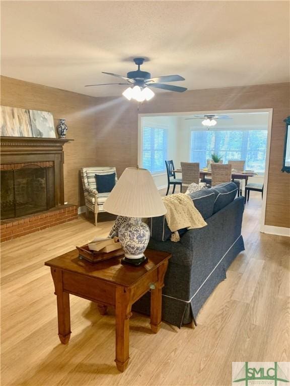 living area featuring ceiling fan, a fireplace, baseboards, and wood finished floors