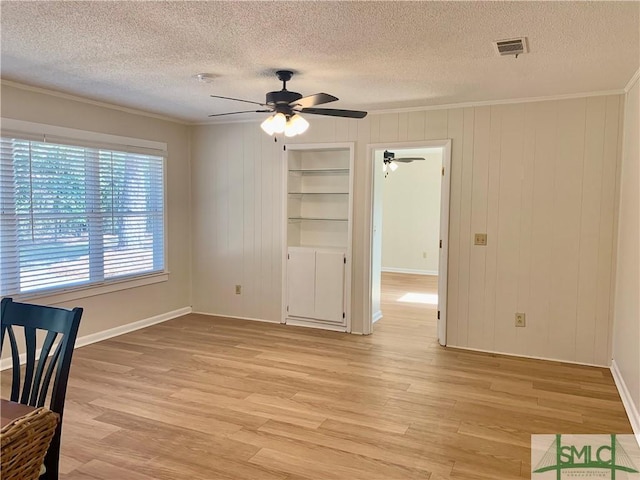 interior space featuring ornamental molding, built in shelves, light wood-type flooring, and visible vents