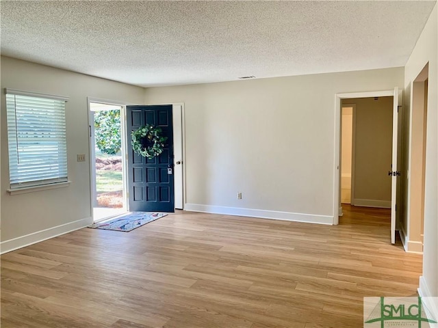 foyer entrance with visible vents, baseboards, light wood-style flooring, and a textured ceiling