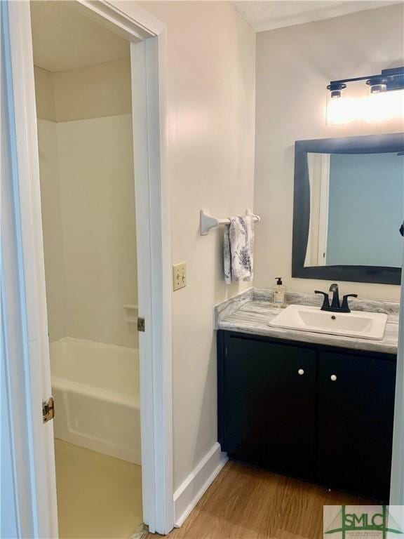 bathroom with wood finished floors, a bathing tub, vanity, and baseboards