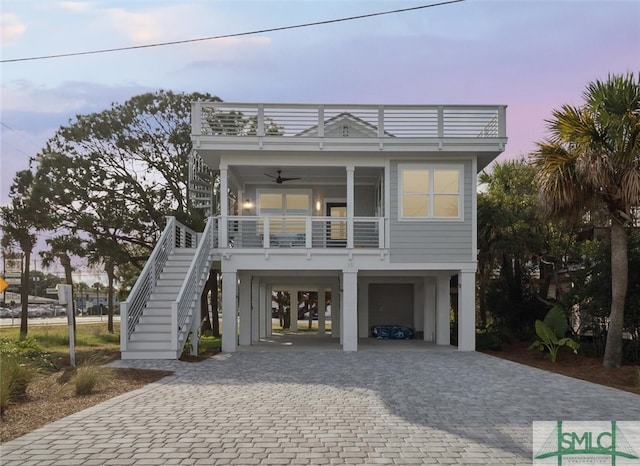 coastal inspired home with ceiling fan, covered porch, stairs, decorative driveway, and a carport