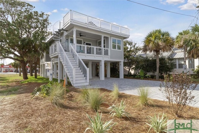 coastal home featuring ceiling fan, covered porch, stairs, decorative driveway, and a carport