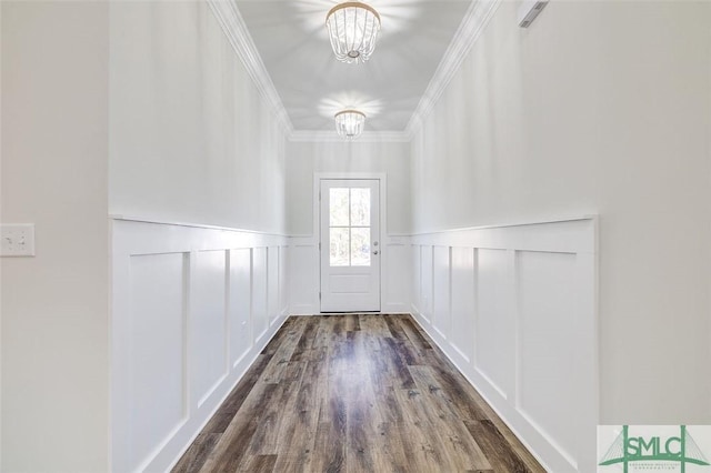 doorway featuring crown molding, a decorative wall, dark wood-style floors, and an inviting chandelier