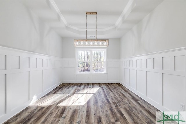 unfurnished dining area featuring crown molding, a tray ceiling, a decorative wall, and wood finished floors