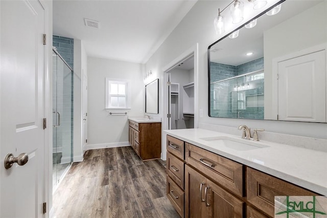 full bath with wood finished floors, two vanities, a sink, and a shower stall