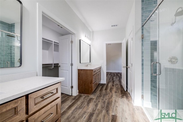 bathroom with wood finished floors, two vanities, a sink, a stall shower, and a walk in closet